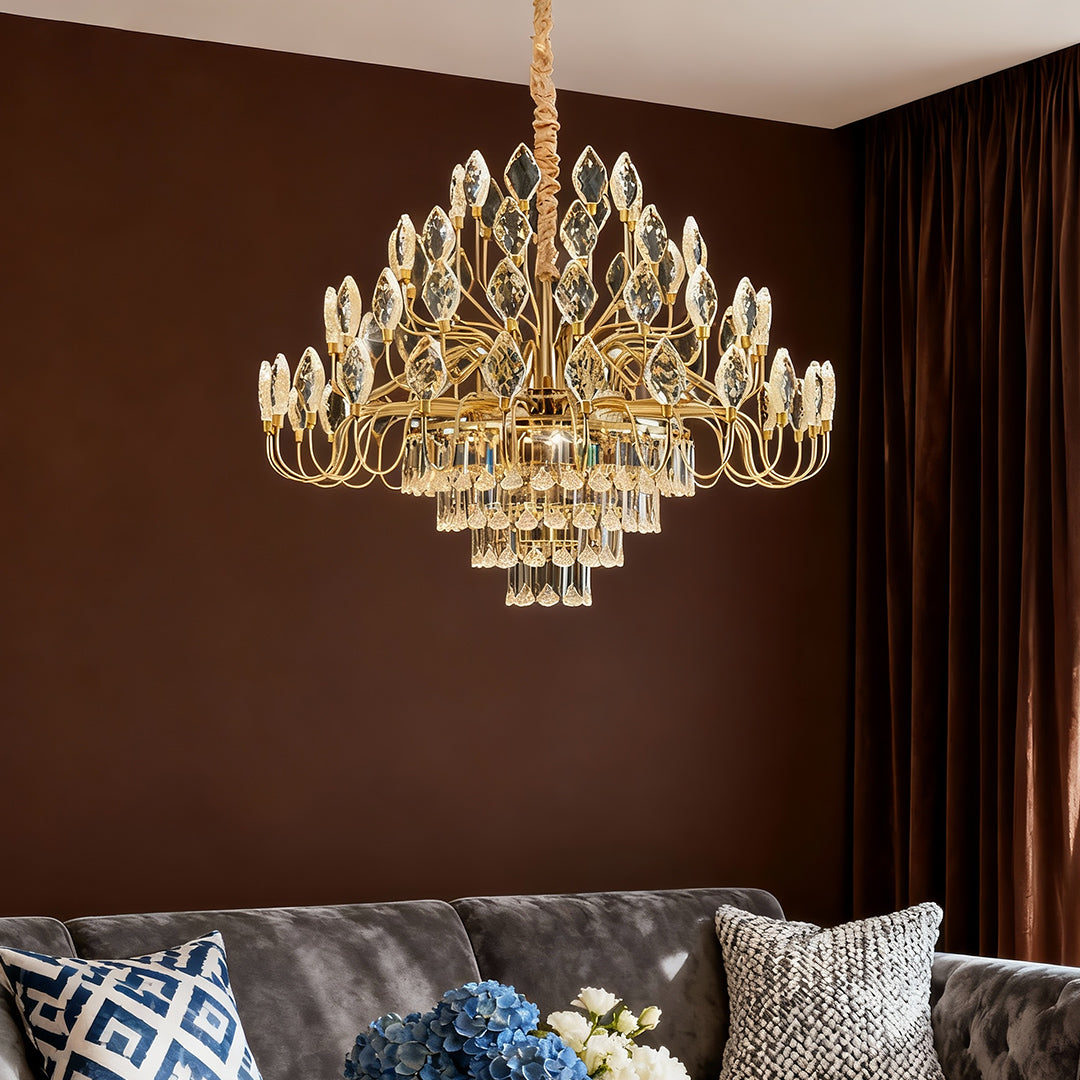 A gold crystal chandelier glowing warmly in a living room with chocolate brown walls and a grey velvet sofa
